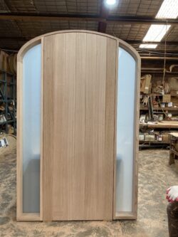 Two natural timber doors with gothic arch tops and decorative detailing, under construction in the Marrickville Joinery workshop.