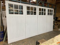 Custom-built white-painted bifold garage door featuring multiple raised timber panels and wide glass sections, crafted at the Marrickville Joinery workshop.