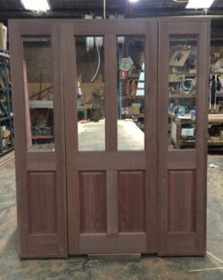 Heritage-style double timber doors with glass panel inserts, stained in a warm tone and ready for installation.
