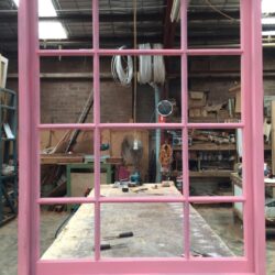Workshop scene showing pink painted door and window frames in various stages of assembly.