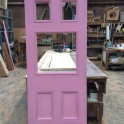 Pink painted four-panel heritage timber door photographed in the workshop.