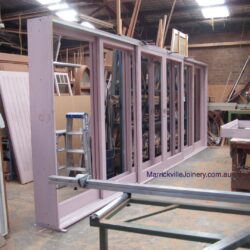 Workshop storage area with multiple completed and in-progress timber components, doors, and frames.