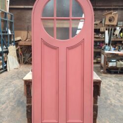 Pink painted heritage entrance door with an arched six-pane glass upper section, characteristic of Federation-era architecture.