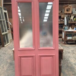 Double pink painted heritage doors featuring glass panel inserts, ready for installation in a residential property.