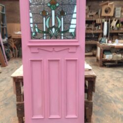 Pink painted heritage door with multiple decorative panels, representing a traditional design commonly used in Victorian-era homes.