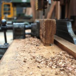 Rough-cut timber block resting on a sawdust-covered workshop floor, capturing the working environment of heritage joinery production.