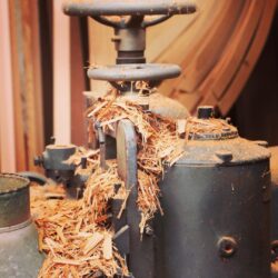 Woodworking drill press or boring machine in the workshop, surrounded by sawdust from active production.
