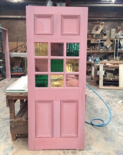 Completed pink painted heritage door with decorative leadlight glass panels, ready for installation in a period home.
