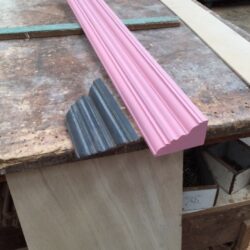 Close-up of a pink painted profiled moulding or cornice edge, showing the precise profile of heritage timber moulding. Pink Moulding Edge Close-Up