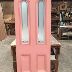 Pink painted heritage door featuring two tall vertical oval glass inserts, a decorative design element common in Victorian homes.